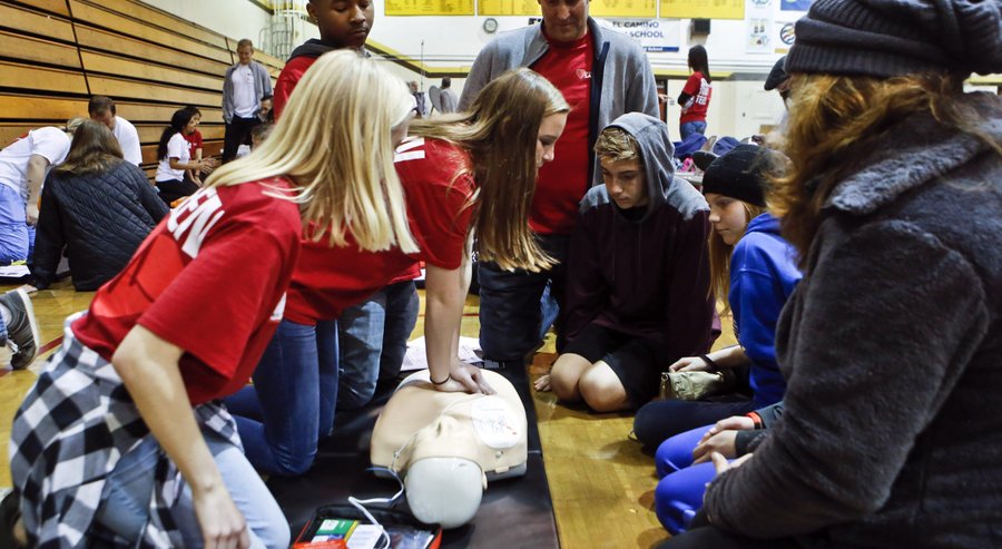 Oceanside teacher Doug Musgrove (top center) looks on as Callie Zellers demonstrated CPR techniques during training for teenagers and their parent at the free youth heart screening at El Camino High School on Sunday. 